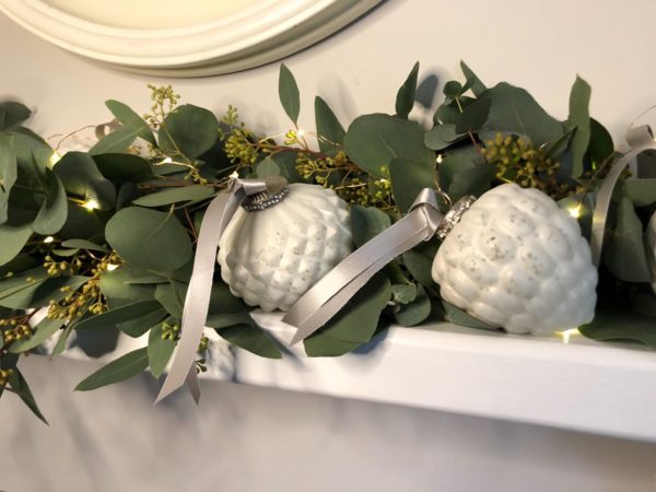 eucalyptus garland with 2 white fir cone shaped babubles nestled into it on a mantlepiece